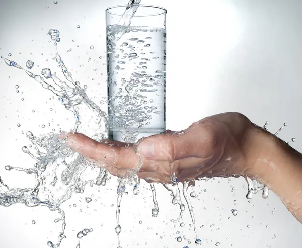 Womans hand holding glass of water splashing