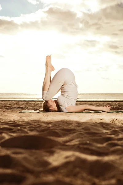 Young beautiful slim woman practices yoga on the beach at sunris