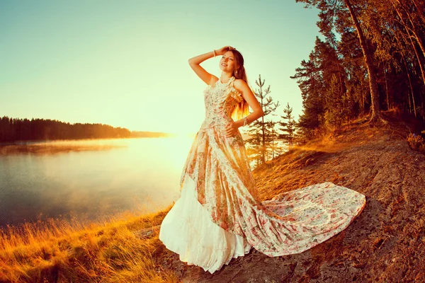 Luxury woman in a forest in a long vintage dress near the lake.