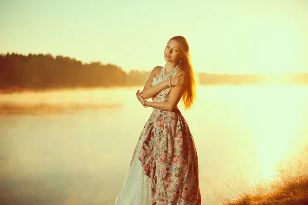 Luxury woman in a forest in a long vintage dress near the lake.