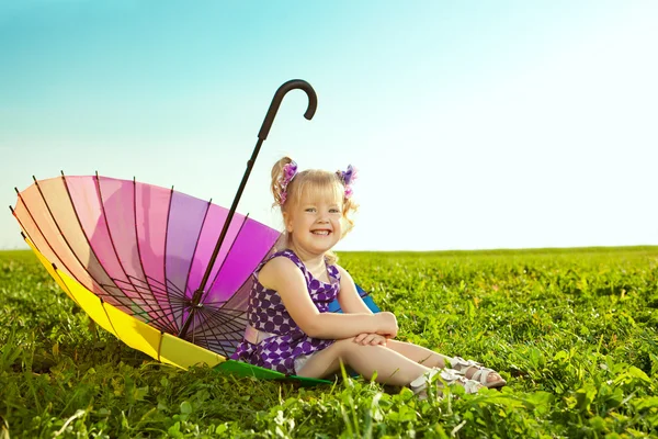 Beautiful little girl with rainbow umbrella on the grass in the