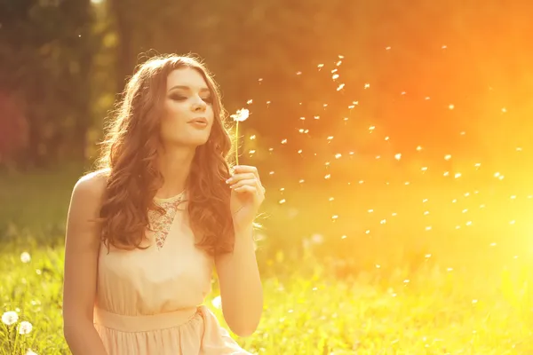 Beautiful young woman blowing a dandelion. Trendy young girl at