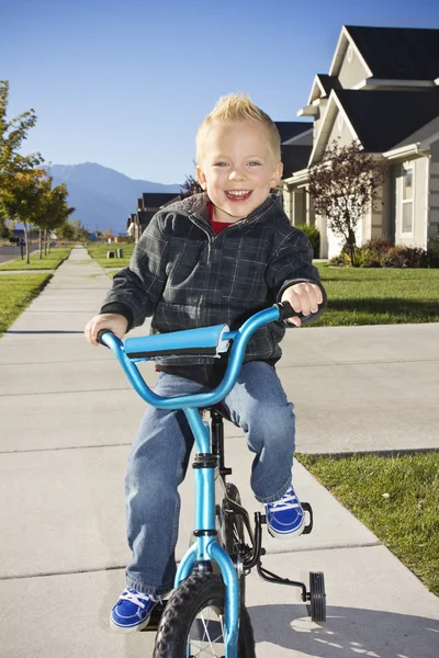 Little boy learning to ride a bike with training wheels