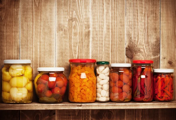 Preserved autumn vegetables on shelf near a wooden wall