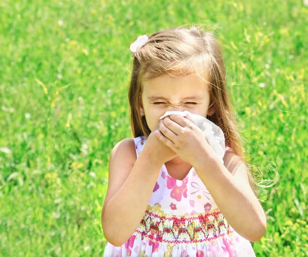 Little girl is blowing her nose on green meadow