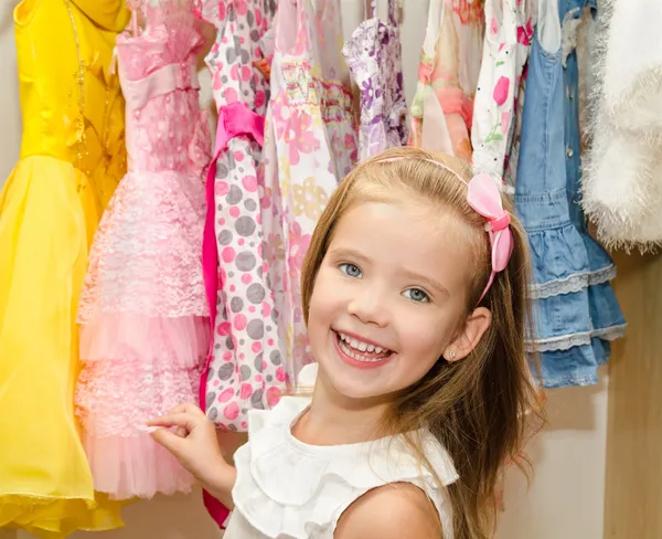 Smiling little girl chooses a dress from the wardrobe