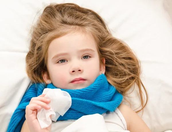 Sick little girl lying in the bed with scarf and tissue