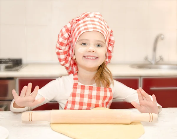 Smiling little girl with chef hat rolling dough