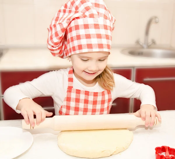 Smiling little girl with chef hat rolling dough
