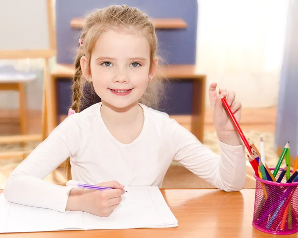 Cute smiling little girl is writing at the desk