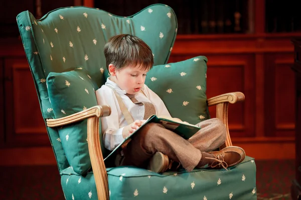 Cute little boy reading book on armchair