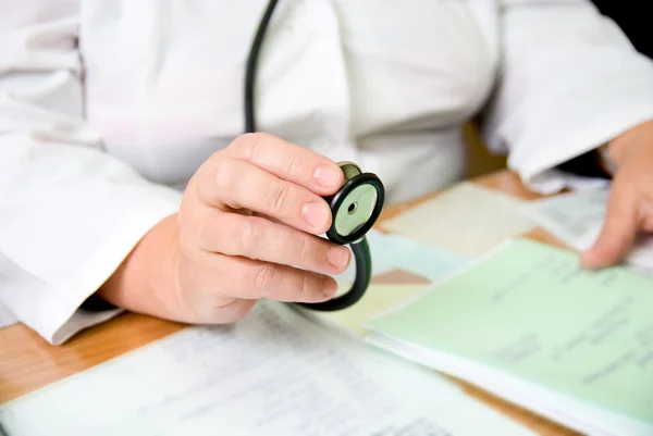 The doctor sits at a table holding a stethoscope in her hand.