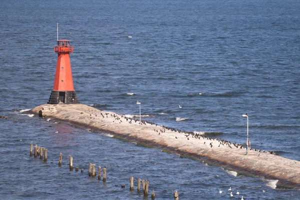 A red lighthouse at the end of a stone pier.