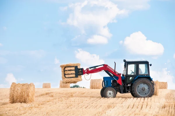 Tractor collecting round bales of straw.