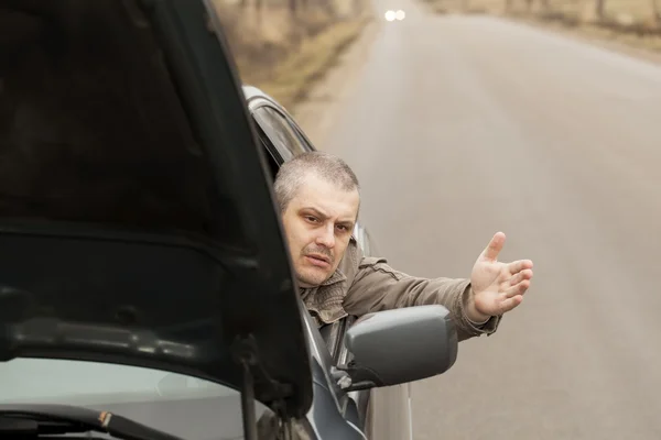 Man sitting in broken car on the road