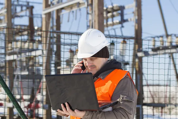 Electrical engineer with computer near the electricity substation