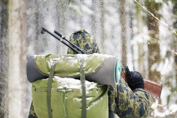 Hunter with optical rifle in winter in snowfall