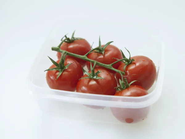 Branch of cherry tomatoes with drops of water in a transparent plastic container