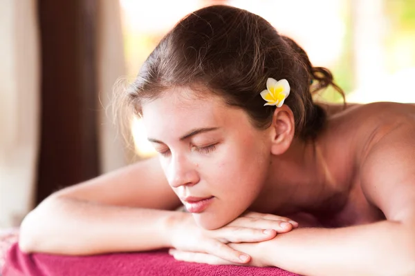 Portrait of beautiful young woman with flower in hair lying in spa