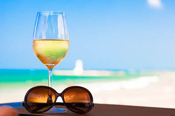 Glass of chilled white wine and sunglasses on table near the beach