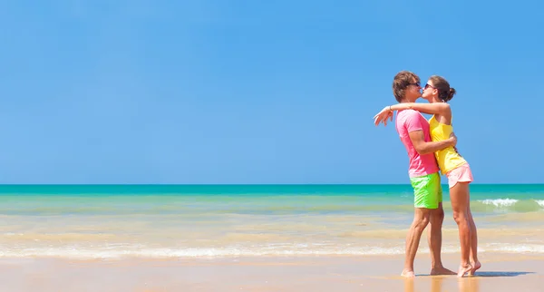 Panoramic view of happy young couple in sunglasses in bright clothes flirting on tropical beach