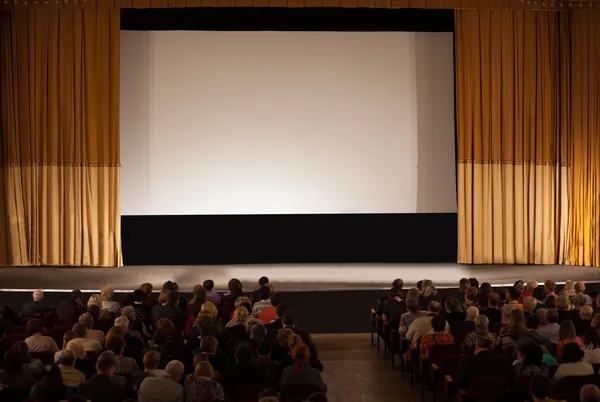 Audience in an auditorium in front of white cinema screen