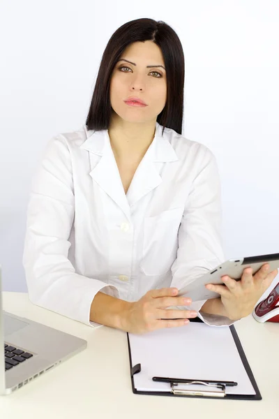 Serious woman doctor working with technology sitting at desk