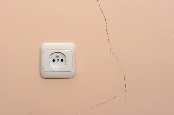 A crack in the wall next to an electrical outlet