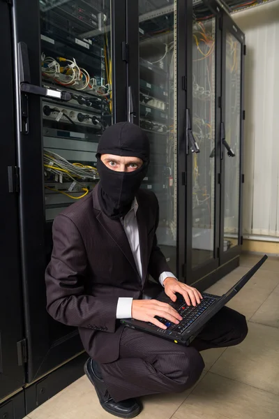 Robber in black mask hack server room downloading data on laptop