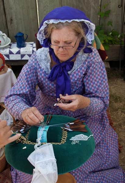 Woman in 19th century costume makes bobbin lace
