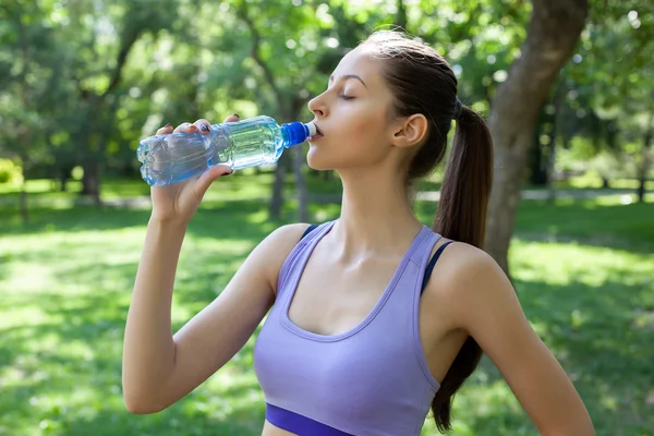 Young beautiful girl drinking water after sport