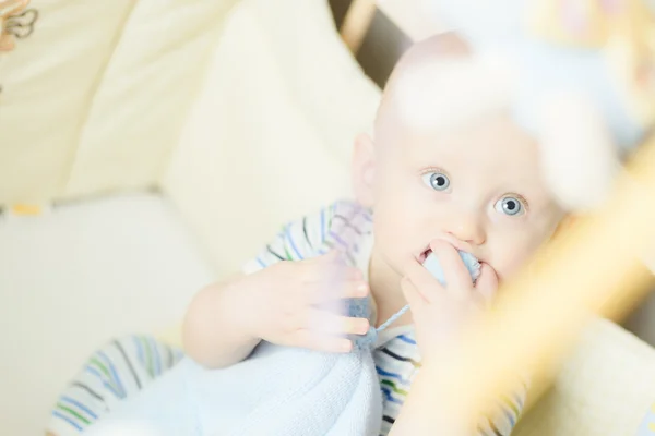 Little baby playing biting his cap when sitting in a small childrens bed