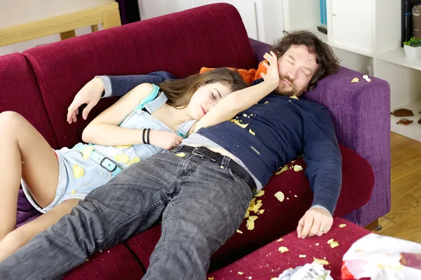 Daughter hugging father on couch sleeping with chaos around