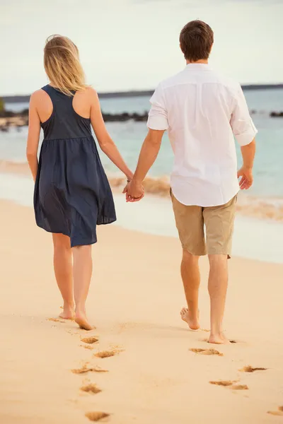 Romantic happy couple walking on beach at sunset. Smiling holdin