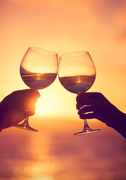 Man and woman clanging wine glasses with champagne at sunset dra