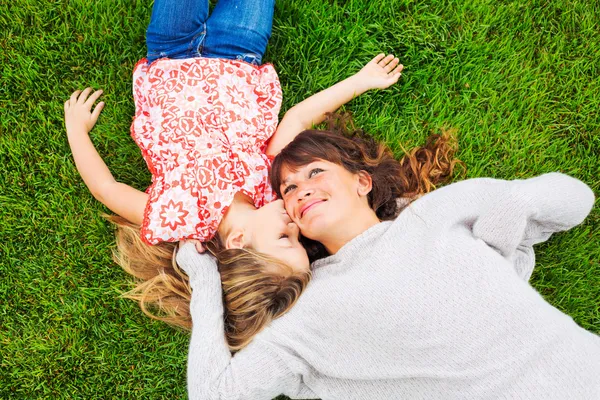 Happy mother and daughter relaxing outside on green grass. Spend