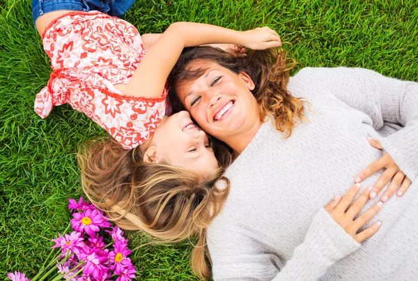 Happy mother and daughter relaxing outside on green grass. Spend