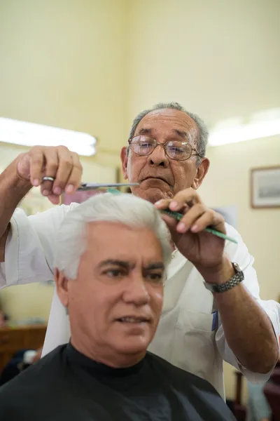 Old barber cutting hair to client in barber shop