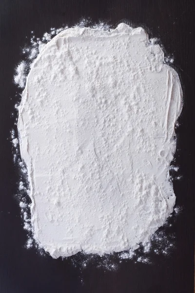 White flour sprinkled on a dark wooden table. top view