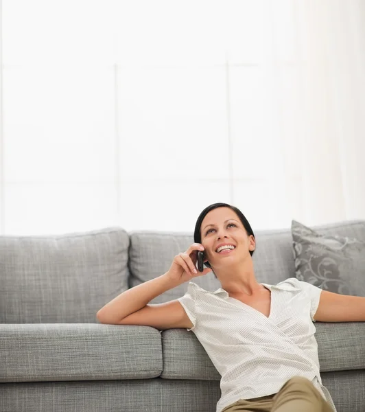 Happy young woman sitting on floor and speaking cell phone