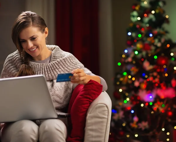 Happy woman with laptop and credit card in front of Christmas tr
