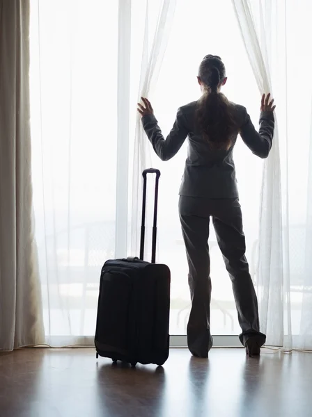 Silhouette of business woman with wheel bag looking into hotel window