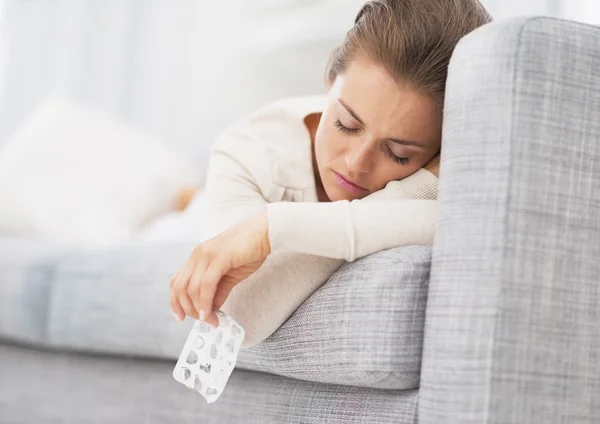 Young woman laying on sofa and holding empty medicine blister pa