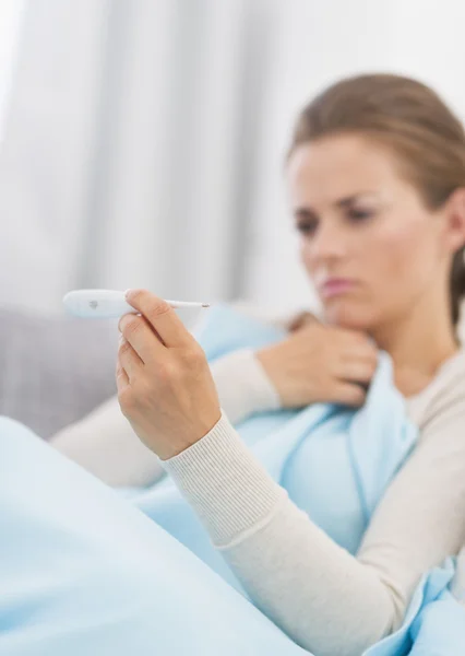 Concerned young woman looking on thermometer