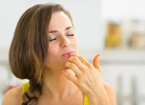 Woman in kitchen licking fingers