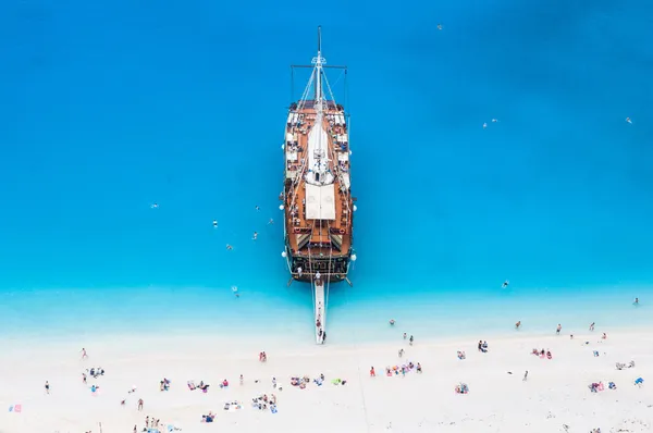 Large sail cruise ship anchored at white sand beach, seen from above