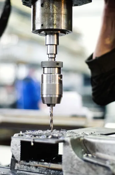 Industrial worker drilling a thin, hole in a metal bar