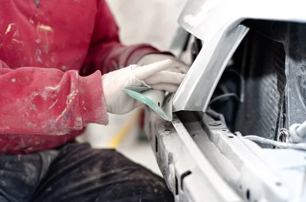 Auto mechanic prepairing the front bumper of a car for painting