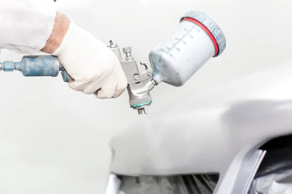 Close-up of a spray paint gun, painting a car. Worker painting the hood of a car
