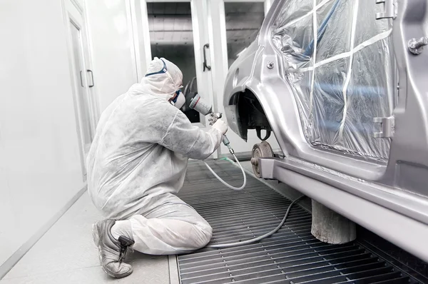 Worker painting a grey car in a special garage
